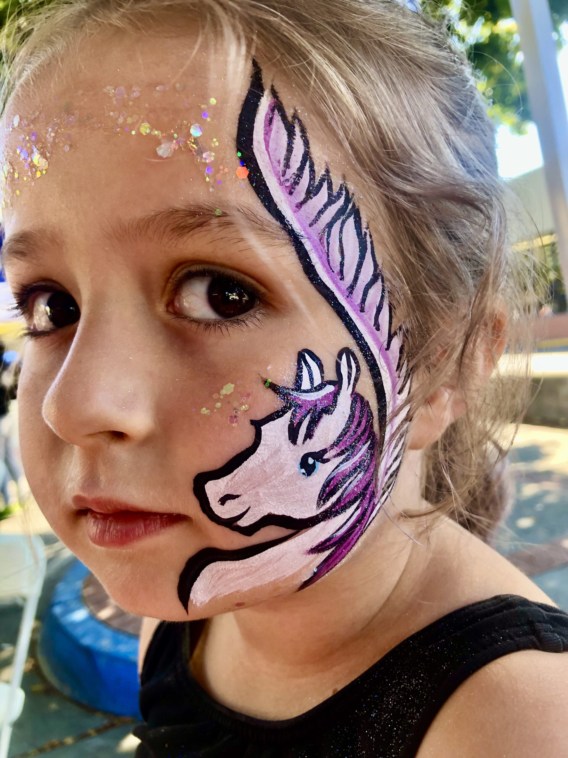 A child with a pink glittery pegasus design on her face